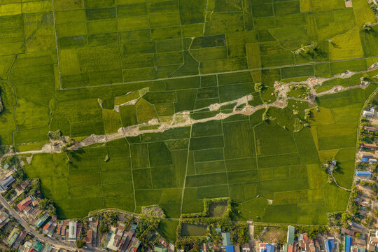 Aerial view of Lak Lake surrounded by vibrant green rice paddies and rural residential areas under warm golden hour light in Lien Son Lak, Dak Lak, Vietnam.