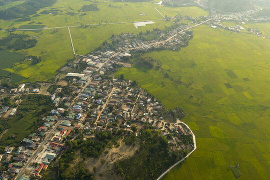 Aerial view of Lak Lake surrounded by lush green rice paddies and residential rooftops in Lien Son Lak, Dak Lak, Vietnam.