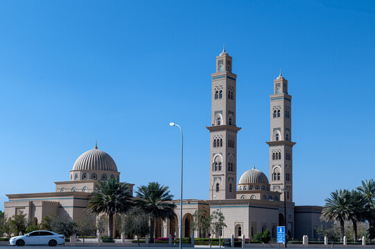 View of a modern mosque with two tall minarets and domes under a clear blue sky in Muscat, Muscat Governorate, Oman.