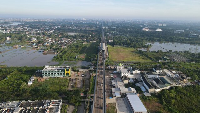 Aerial view of the Jakabaring area with the light rail transit line crossing green landscapes, buildings, and water bodies in Kecamatan Seberang Ulu I, Sumatera Selatan, Indonesia.