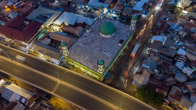 Aerial view of the illuminated Tamale Central Mosque with its green dome and minarets, situated next to a busy highway with light trails from traffic in Tamale, Northern Region, Ghana.