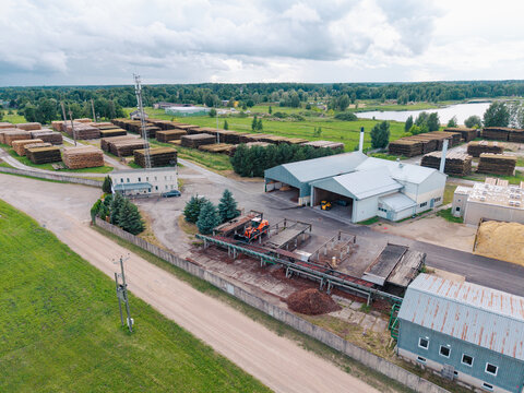 Aerial view of a lumber mill facility featuring large stacks of logs, industrial processing buildings, and heavy machinery in a rural landscape in Brankas, Jelgava Municipality, Latvia.
