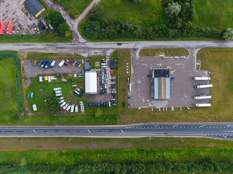 Aerial view of a gas station and a used car dealer with parked vehicles and trucks situated along a highway in Cenu pagasts, Jelgavas novads, Latvia.