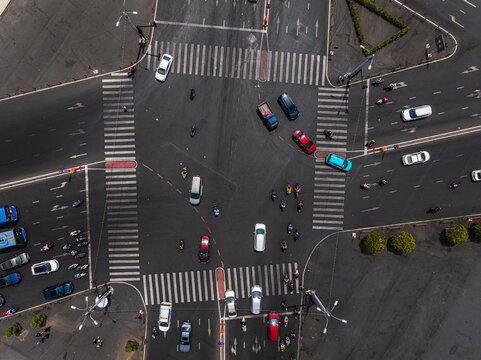 Aerial view of a busy urban intersection with cars, motorcycles, and scooters navigating the crosswalks and lanes under bright daylight, Vietnam.