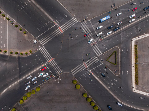 Aerial view of a busy road intersection with cars and motorcycles navigating through crosswalks on asphalt roads in Vietnam.