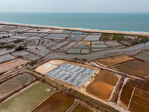 Aerial view of salt production ponds with varying water colors and textures along the coastline in Vietnam.