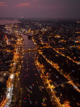 Aerial view of Hoi An Ancient Town at night, featuring the Thu Bon River illuminated by colorful lanterns, traditional architecture, and small boats in Vietnam.