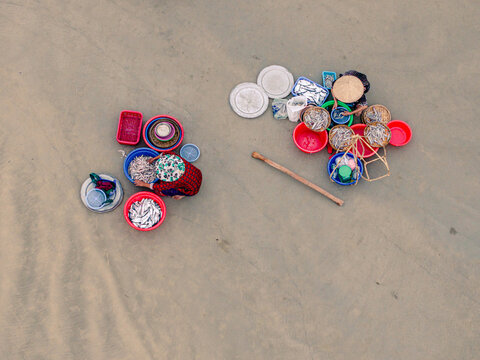 Aerial view of two women sorting fresh fish in colorful plastic basins on a sandy beach in Vietnam.