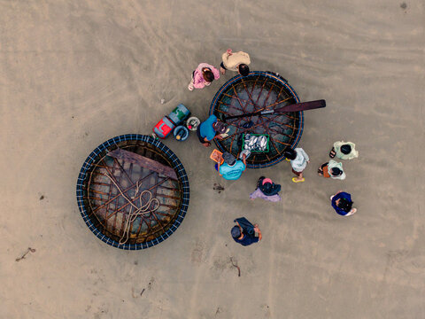 Aerial view of fishermen working with traditional basket boats on a sandy beach in Vietnam.