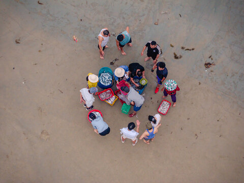 Aerial view of fishermen sorting freshly caught fish in colorful baskets on a sandy beach in Vietnam.