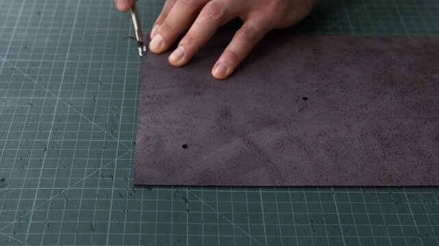 Artisan chamfering dark leather edges with a skiving tool on a green cutting mat in a workshop