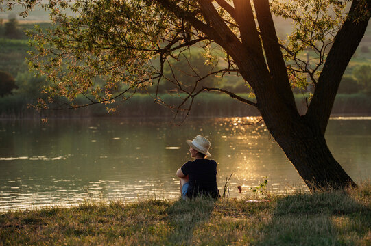 Woman enjoying solitude by the lake in warm summer sunset.