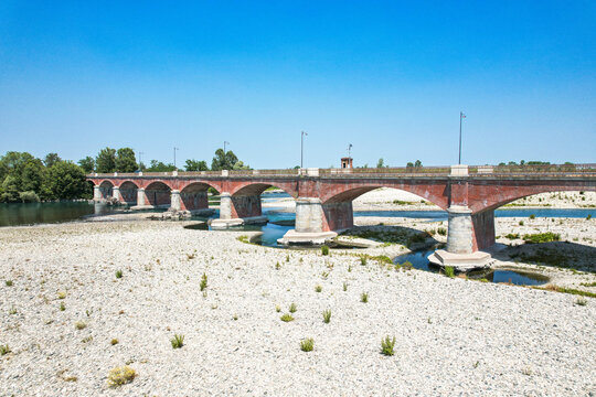 Aerial view of the historic brick Ponte Crescentino spanning the dry riverbed of the Po River during a severe drought in Verrua Savoia, Piemonte, Italy.
