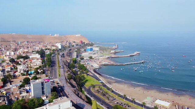 Aerial view of Malecon de Chorrillos, coastal road, beach, and fishing boats in the bay of Lima, Provincia de Lima, Peru.