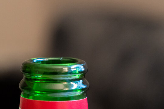 Green glass bottle neck close-up with open mouth and rolled lip, macro detail of empty beer bottle on blurred dark background, concept of beverage packaging