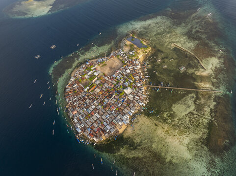 Aerial view of Pulau Mesa, a densely populated island village surrounded by turquoise coral reefs and clear blue water in Kecamatan Komodo, Nusa Tenggara Timur, Indonesia.