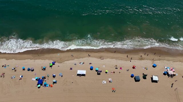 Aerial view of Will Rogers State Beach with colorful umbrellas and people relaxing on the sand along the Pacific Ocean coastline in Los Angeles, California, United States.