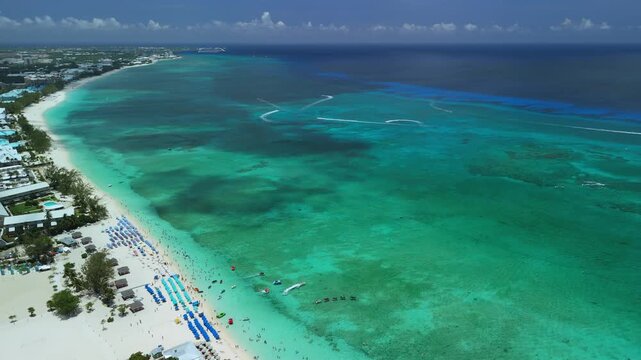 Aerial view of Grand Cayman beach with white sand, rows of umbrellas, and clear turquoise water in the Cayman Islands.