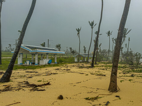 San Jose, Tinian, Northern Mariana Islands - 06 July 2026: View of Super Typhoon Bavi aftermath with damaged palm trees, scattered debris, and empty park shelters under a dark, stormy sky.