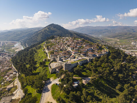 Aerial view of the historic Berat Castle and the surrounding old town with traditional stone houses, lush green hills, and mountains in the background in Berat, Berat County, Albania.