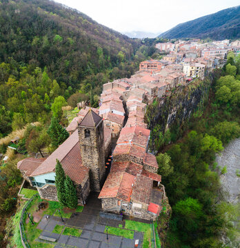 Aerial view of the historic village of Castellfollit de la Roca perched on a basalt cliff with stone buildings and a church bell tower in Castellfollit de la Roca, Catalunya, Spain.