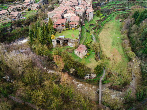 Aerial view of the historic village of Rupit with stone houses, terracotta rooftops, and a winding river flowing through the lush green landscape in Rupit, Catalonia, Spain.