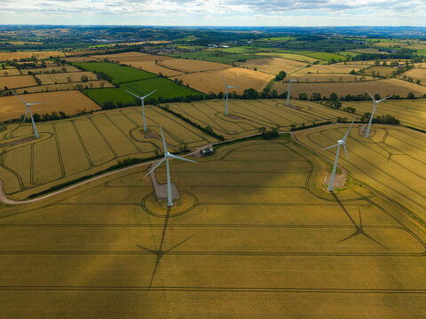 Aerial view of wind turbines standing in golden wheat fields with long shadows cast across the rural landscape in Melton Mowbray, England, United Kingdom.