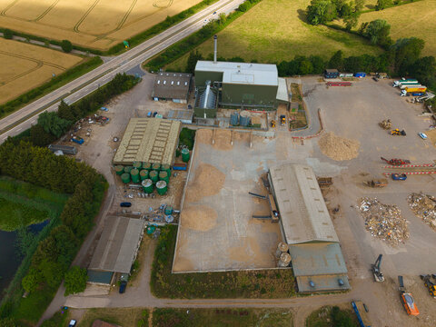 Aerial view of Widmerpool Biomass Powerplant with large wood chip piles, industrial storage sheds, and surrounding agricultural fields in Widmerpool, England, United Kingdom.