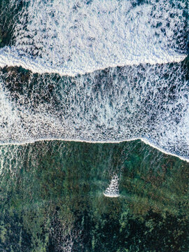 Aerial view of turquoise ocean waves crashing over a coral reef in the Indian Ocean near the coast of Mauritius.