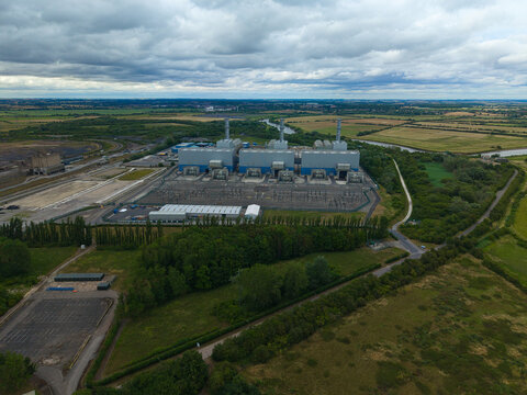 Aerial view of West Burton Power Station featuring large industrial buildings and chimneys set amidst green fields and rural landscape in West Burton, England, United Kingdom.