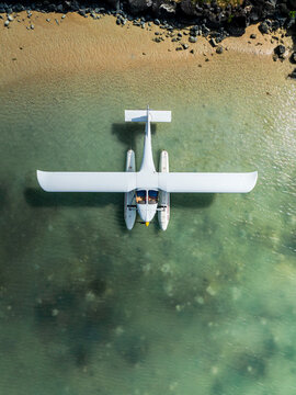 Aerial view of a white seaplane floating on clear turquoise water near a sandy beach in Mauritius.