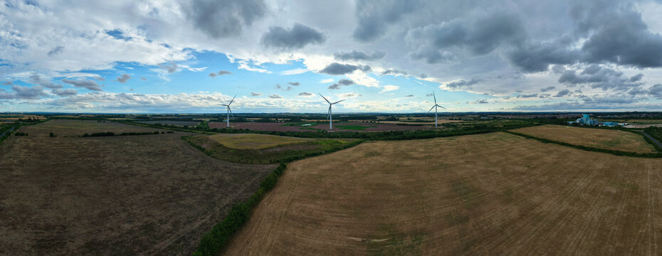 Aerial view of Hawton Wind Farm with wind turbines standing in vast agricultural fields under a cloudy sky in Newark, England, United Kingdom.