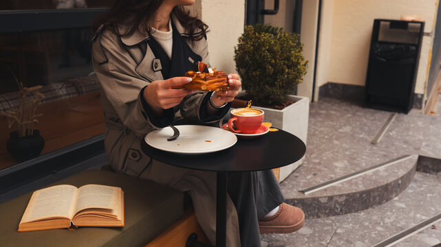 Woman enjoying a pastry and coffee at an outdoor cafe table with a book