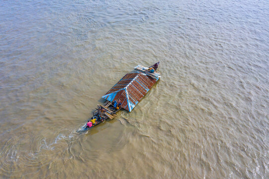 Bogura, Bangladesh - 29 August 2021: Aerial view of a small boat transporting a salvaged house roof across the floodwaters of the Jamuna River near Sariakandi, with people on board.