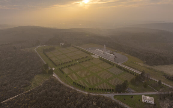 Aerial view of the Douaumont Ossuary and its military cemetery at sunset, with rows of crosses and trees in the rolling hills of Douaumont-Vaux, Grand Est, France.