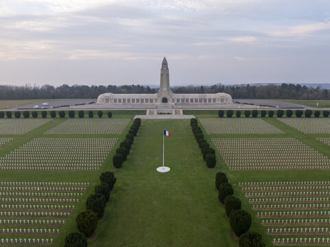 Aerial view of the Douaumont Ossuary, a historic memorial site surrounded by rows of white crosses in the military cemetery, with a French flag, Douaumont-Vaux, Grand Est, France.
