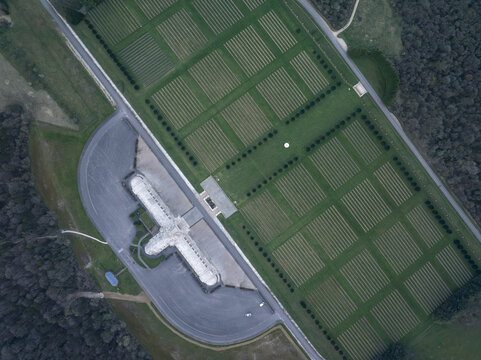 Aerial view of the Douaumont Ossuary and the surrounding military cemetery with rows of white crosses set in green grass near the forest in Douaumont-Vaux, Grand Est, France.