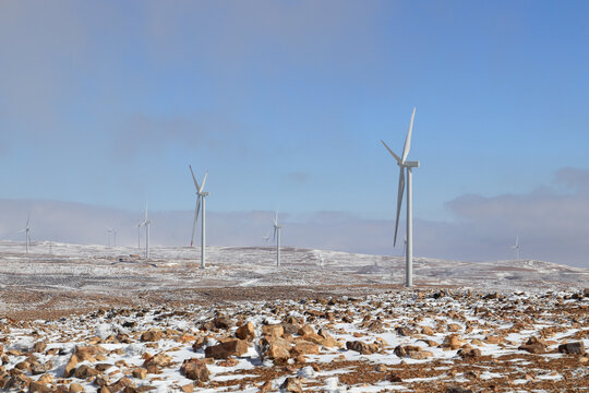 View of wind turbines in a rocky, snow-covered landscape, Al-Qadisiya, Tafilah Governorate, Jordan.