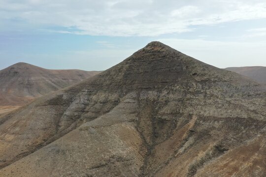 Aerial view of the volcanic landscape around Mirador de Vallebron, featuring rugged mountain slopes, arid terrain, and rocky textures in La Oliva, Canary Islands, Spain.