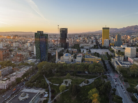 Aerial view of the modern skyline and historic architecture of Tirana, including the Ethem Bey Mosque, surrounded by lush parks and urban streets at sunset in Tirana, Tirana County, Albania.