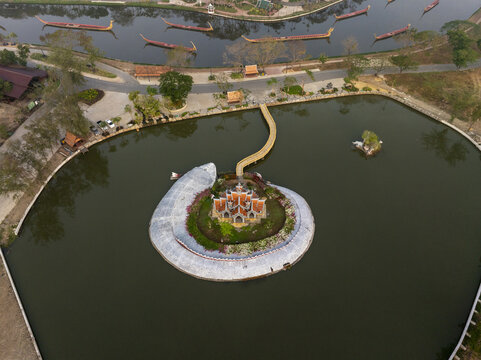 Aerial view of the Sumeru Mountain structure surrounded by a circular moat with a pedestrian bridge, traditional Thai boats, and greenery in Phraeksa, Samut Prakan, Thailand.