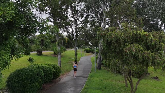 Female runner in activewear burning calories with a cardio workout. Sporty woman jogging running on city park bridge outdoors. Woman exercising with earphones on in the morning. Copy space Stock Photo