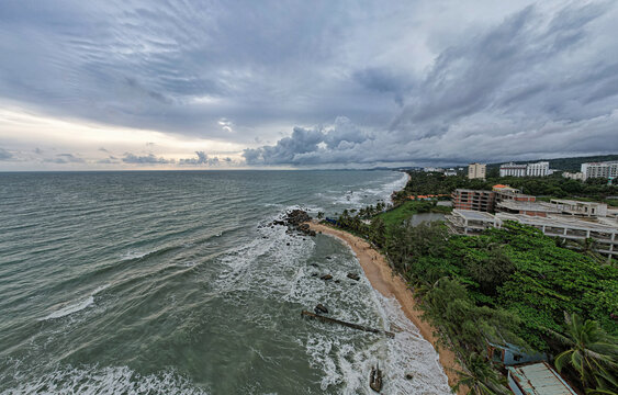 Aerial view of Long Beach Bai Truong with rocky shoreline, lush palm trees, and coastal buildings under a dramatic cloudy sky in Phu Quoc, Kien Giang, Vietnam.