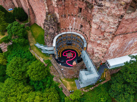 Aerial view of Heidelberg Castle featuring a modern stage structure nestled within ancient red sandstone walls, surrounded by lush green trees in Heidelberg, Baden-Wurttemberg, Germany.