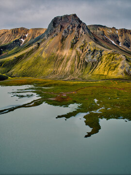 Aerial view of the colorful volcanic mountains and mossy landscape of Landmannalaugar with a glacial lake in the foreground, Hella, Rangarthing ytra, Iceland.