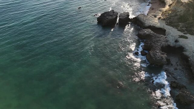 serene rocky coastline aerial view of still ocean and rocky shore with blue and green hues and clean natural landscape for nature and landscape editorial and educational use cases.