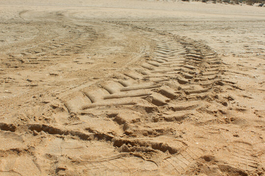 Tire tracks crossing soft sand, creating textured patterns beneath bright natural sunlight outdoors.