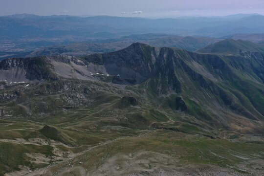Aerial view of Monte Corvo in the Gran Sasso massif featuring rugged rocky slopes and green alpine meadows in L'Aquila, Abruzzo, Italy.