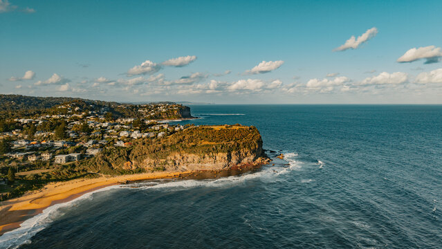 Aerial view of the coastal headland and beach at Mona Vale, featuring residential houses on the cliffs, golden sand, and the blue Pacific Ocean in Mona Vale, New South Wales, Australia.
