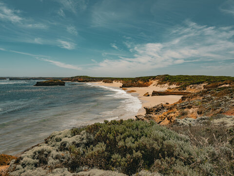 View of the rugged coastline along the Great Ocean Road with sandy beaches, rocky cliffs, and native coastal vegetation under a bright blue sky in Lorne, Victoria, Australia.
